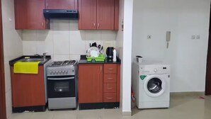 A compact kitchen with a gas stove, oven, and a washing machine. - Horizon Towers Residence Apartment  ★ (Ajman)