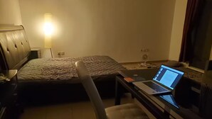 A hotel room with a bed, a desk with a laptop, a chair, and a bedside table. - Horizon Towers Residence Apartment  ★ (Ajman)