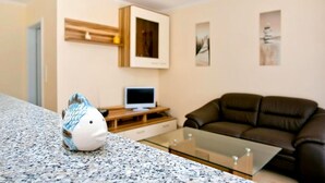 A modern living room with a granite countertop, a brown leather sofa, a flat-screen TV on a wooden stand, and a small fish figurine.