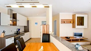 A modern kitchen with white cabinets, a wooden dining table, and a TV on a wooden stand.
