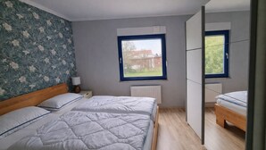 A bedroom with two beds, a radiator, a window with a view, and a wall with floral wallpaper.
