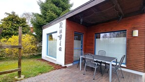A wooden building with a sign reading 'Rugi a' and a patio with a table and chairs.