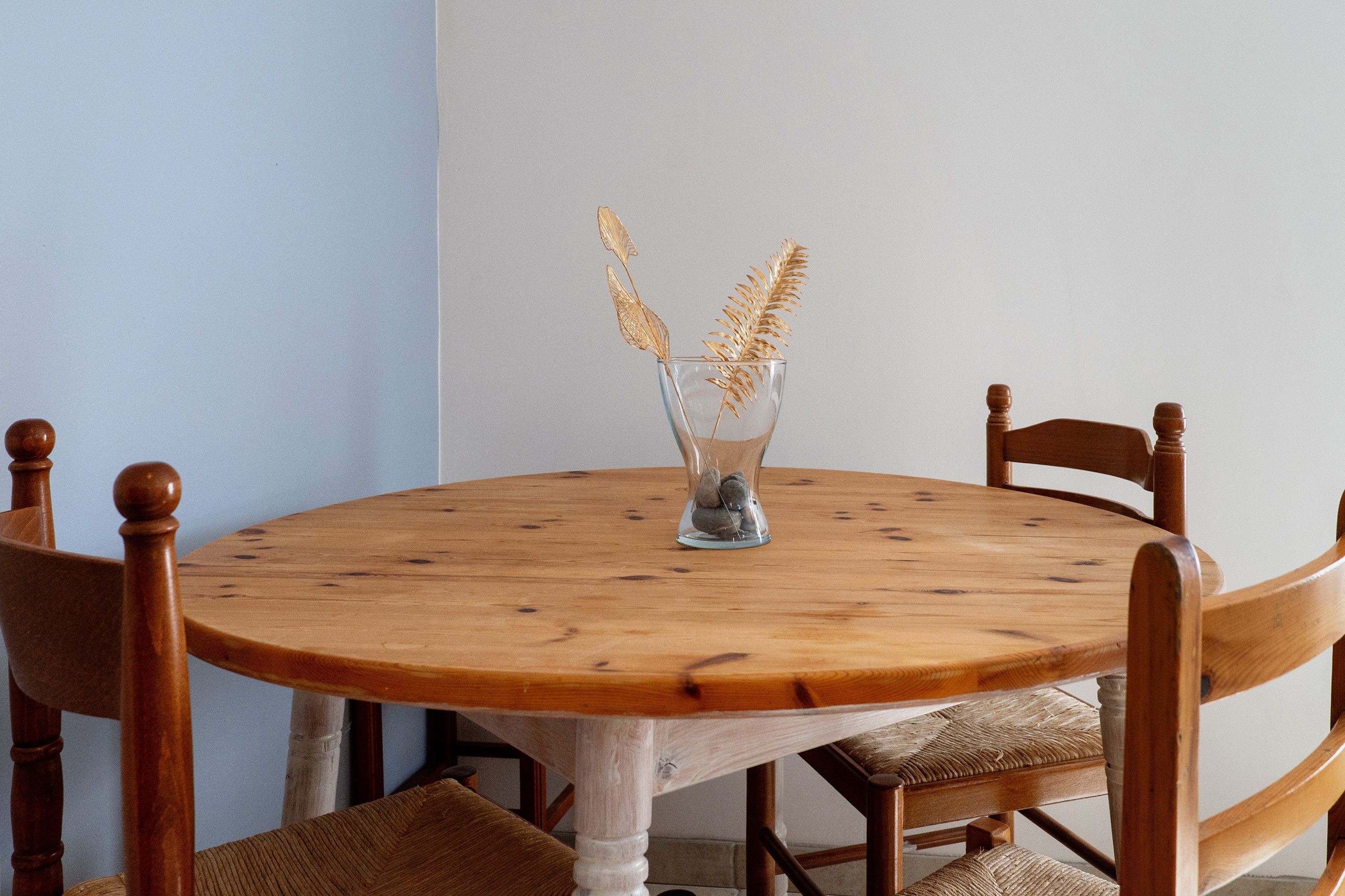 Ein runder Holztisch mit einer Glaskaraffe, die goldene Dekorationen enthält, umgeben von Holzsesseln mit gepolsterten Sitzen.