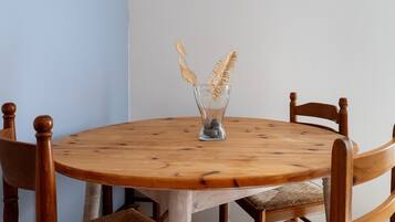 A round wooden table with a glass vase containing golden decorative elements, surrounded by wooden chairs with cushioned seats.
