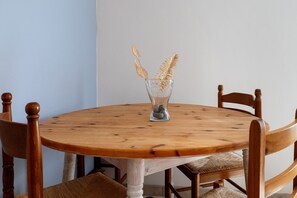 Een ronde houten tafel met een glazen vaas met gouden decoratieve elementen, omringd door houten stoelen met beklede zitplaatsen.