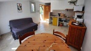 Een gezellig compacte ruimte met een bank, een eettafel, een kitchenette en een deur naar een buitenruimte.