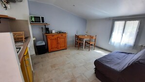 Een compacte kamer met een kitchenette, een eettafel met stoelen, een bed en een raam met gordijnen.