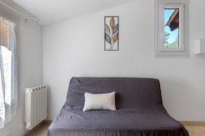 Ett rum med en säng, ett element, ett fönster med utsikt över en byggnad och ett inramat konstverk på väggen.