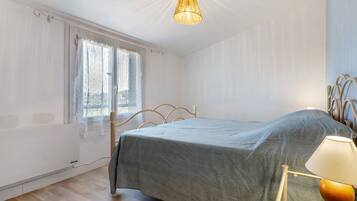 A bedroom with a bed, a window with curtains, a hanging light fixture, and a radiator.