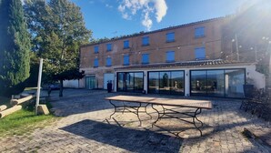 Een gebouw met een pannendak, meerdere ramen en een overdekt terras met een tafel en stoelen.