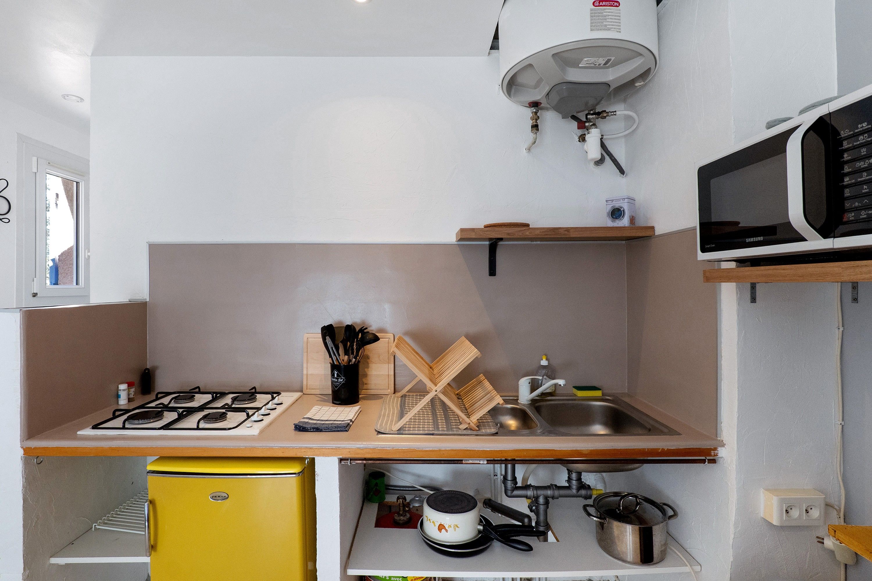 A compact kitchen with a gas stove, a yellow refrigerator, a microwave, and a sink.