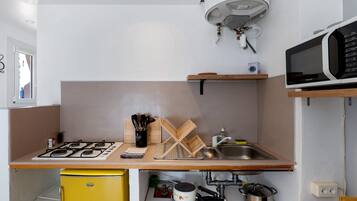 A compact kitchen with a gas stove, a yellow refrigerator, a microwave, and a sink.