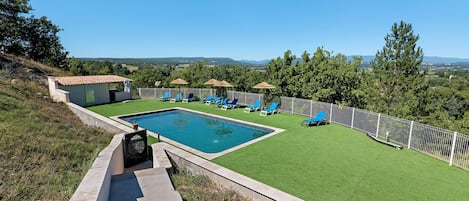 A swimming pool with a surrounding deck, a small building, and a view of the countryside.