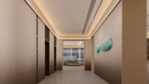 Un couloir moderne avec une bouche d’aération au plafond, une vue sur l’intérieur d’un bâtiment et un mur orné d’œuvres d’art abstraites.
