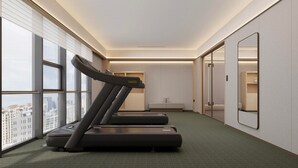 Une chambre d’hôtel équipée d’un tapis de course, d’un lit, d’une petite table et d’une grande fenêtre donnant sur la ville.