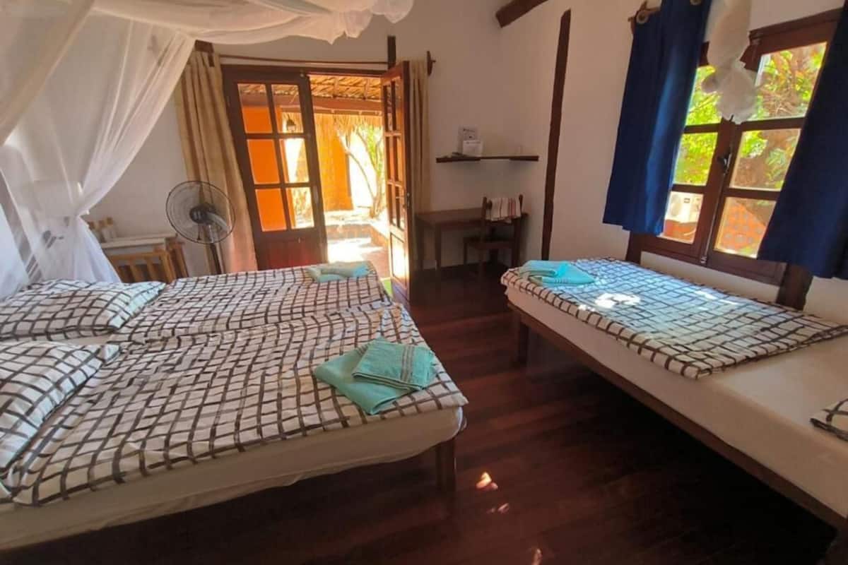 A room with two beds, a fan, a desk, and a window with curtains.