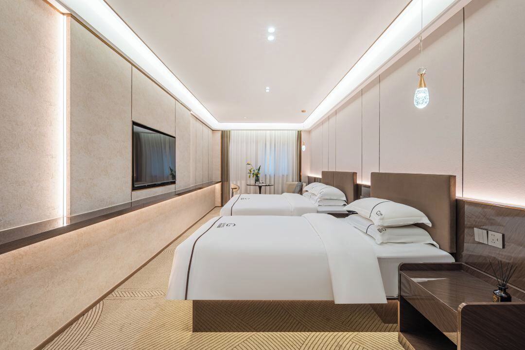 Une chambre d’hôtel avec deux lits, une télévision, une table de chevet et une petite table avec une lampe.