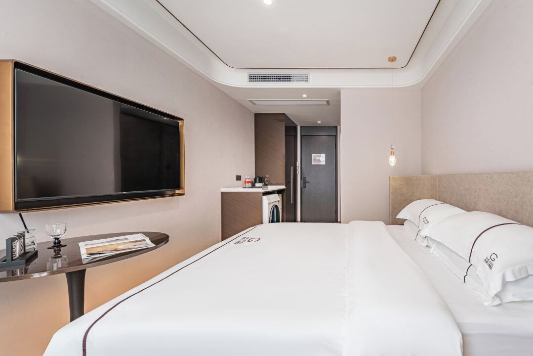 Une chambre d’hôtel avec un lit, une télévision, une petite table avec un verre et une porte donnant sur une salle de bain.