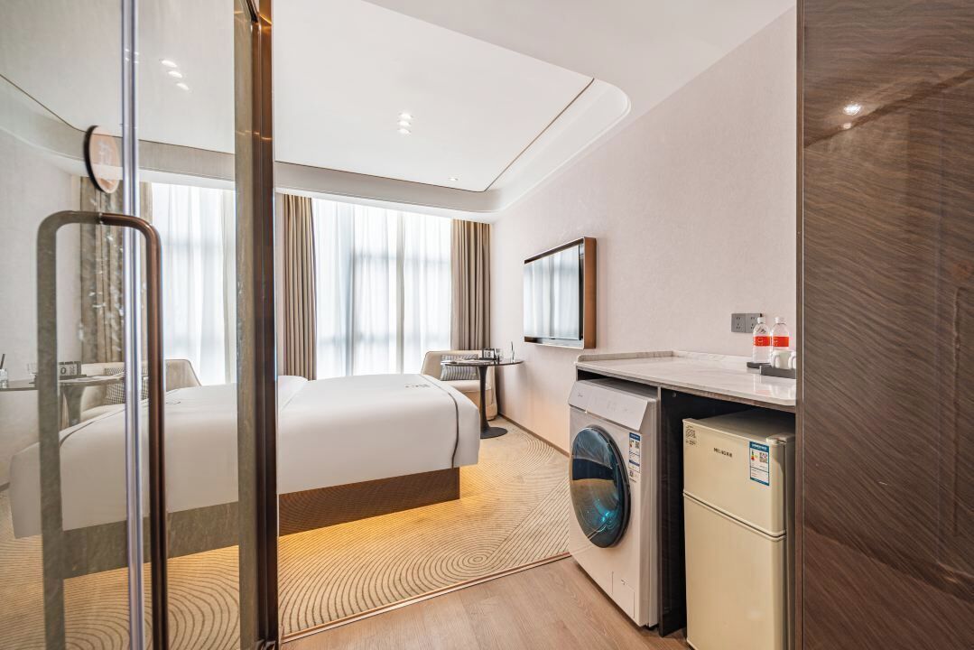 Une chambre d’hôtel avec un lit, un lave-linge, un miroir et une fenêtre avec des rideaux.