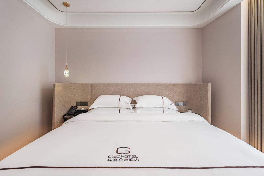 A hotel room with a bed, a nightstand, a telephone, and a hanging light fixture.