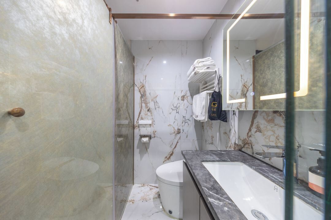 Een moderne badkamer met een marmeren wand, een wit toilet, een wastafel en een glazen douchecabine.
