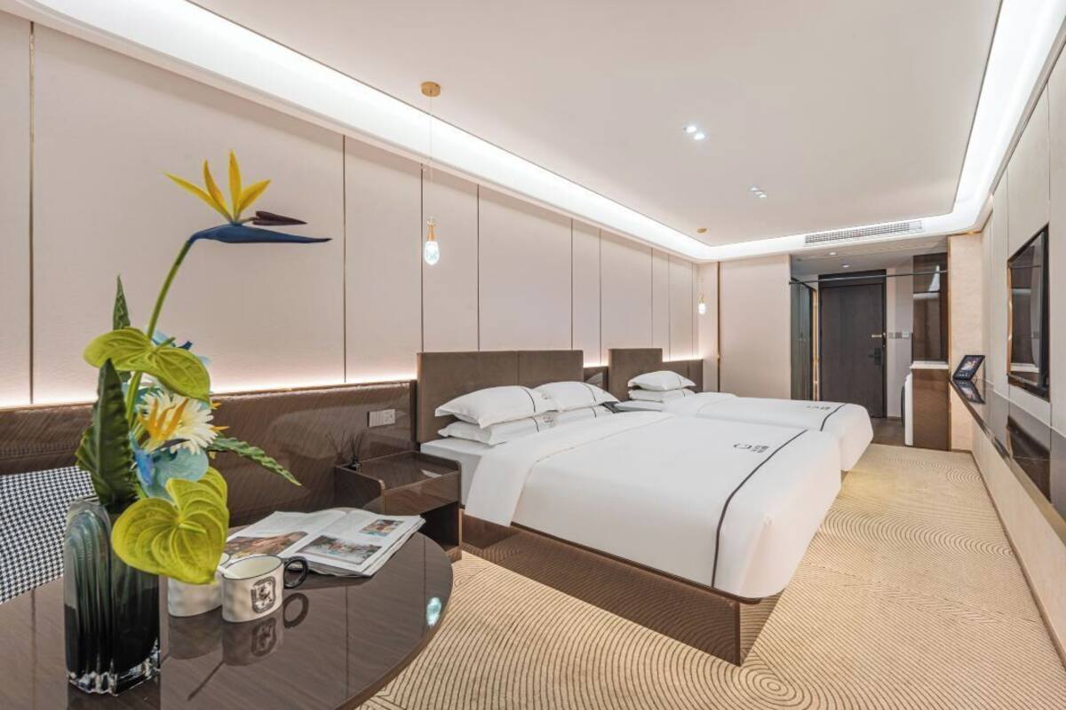 Una habitación de hotel moderna con una cama grande, mesitas de noche, un escritorio y una planta decorativa.