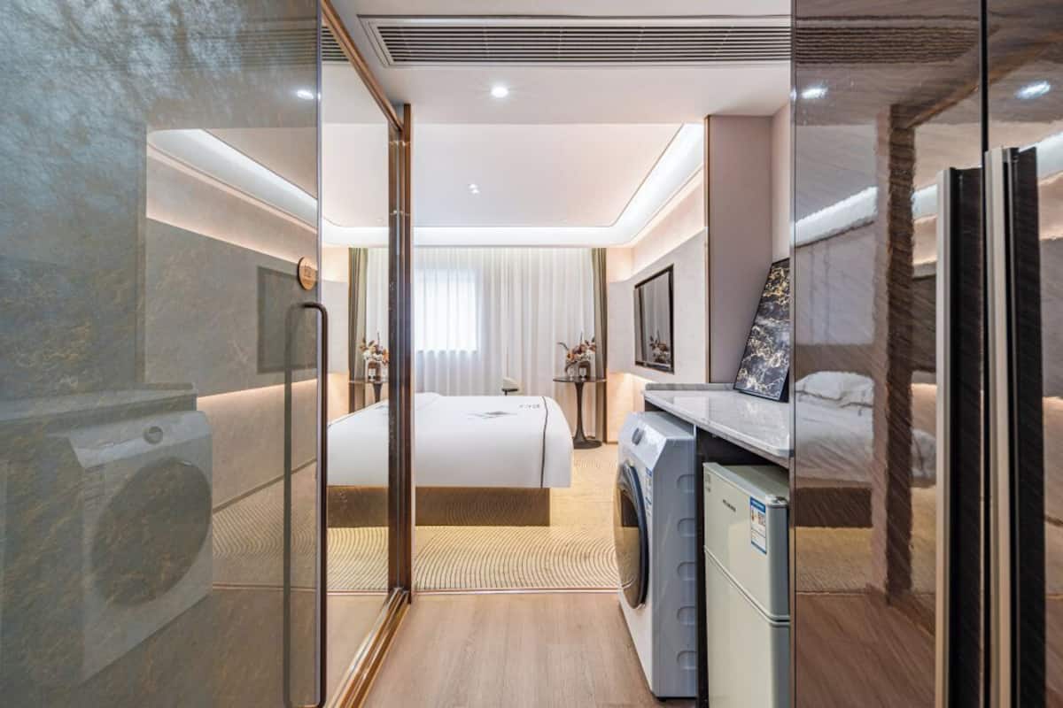 Una habitación de hotel moderna con una cama, una lavadora, una mesita y un espejo.