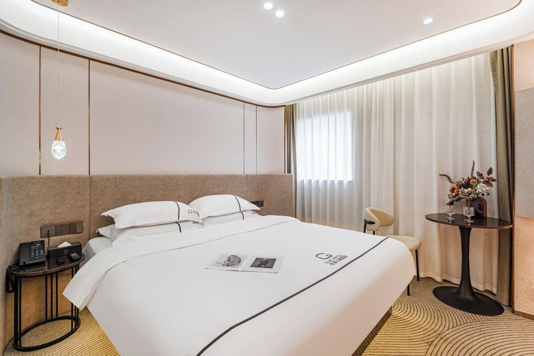 Habitación de hotel con una cama grande, mesita de noche, lámpara y una pequeña mesa con flores.
