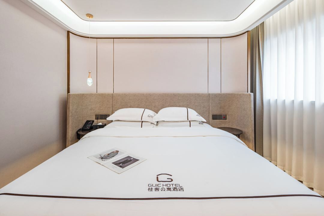 A hotel room with a neatly made bed, a bedside table with a phone, and a window with curtains.