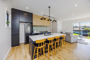A modern kitchen with a central island, bar stools, a refrigerator, and a dining area with a sofa. - Modern 4BR Coastal Stay /Sea Views & Walk to Beach (Torbay)