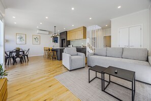 A modern living room with a sofa, coffee table, and dining area with chairs and a table. - Modern 4BR Coastal Stay /Sea Views & Walk to Beach (Torbay)