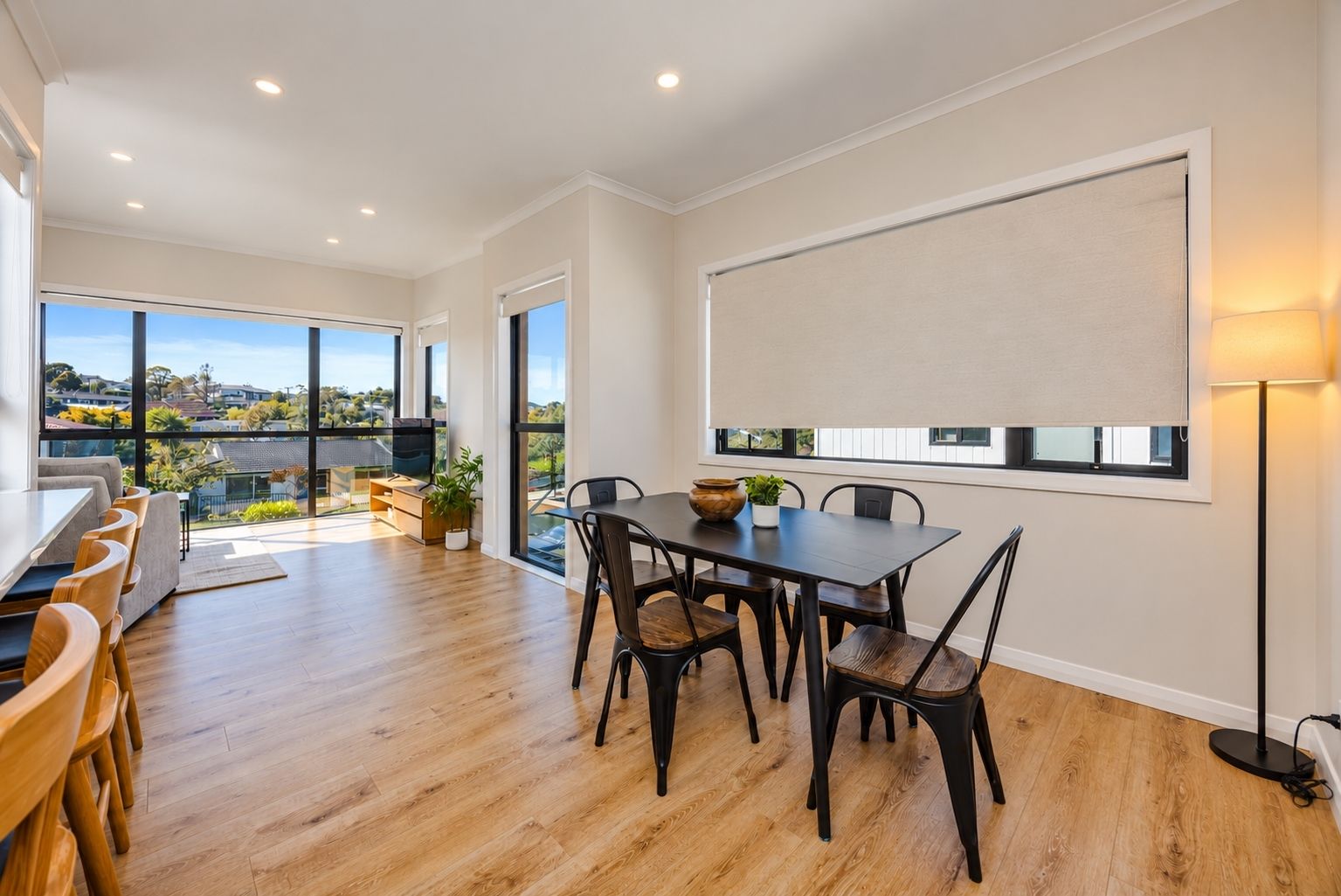 A modern dining area with a wooden table and chairs, a large window with a view, and a ceiling with recessed lighting.