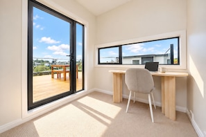 A room with a desk, chair, and large windows offering a view of a deck and buildings. - Modern 4BR Coastal Stay /Sea Views & Walk to Beach (Torbay)