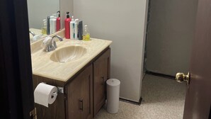 Un baño con lavamanos, espejo, artículos de aseo y retrete.