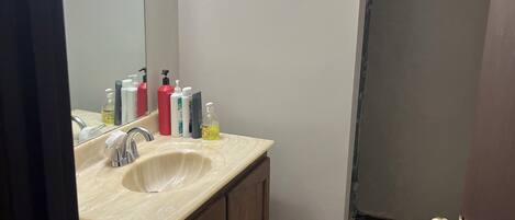 A bathroom with a sink, mirror, toiletries, and a toilet.