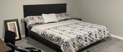 A bedroom with a bed, a treadmill, and a framed picture on the wall.