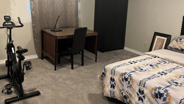 Un dormitorio con cama, escritorio, silla, cinta de correr y armario.