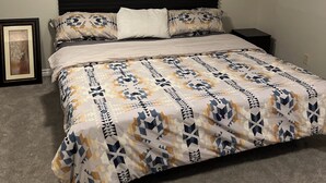 Un dormitorio con una cama, cabecera, mesita de noche, un cuadro enmarco y una lámpara en el techo.