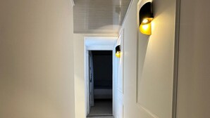 Un corridoio con pareti bianche, pavimento piastrellato e due lampade fissate al muro.