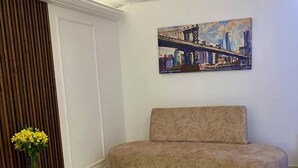 Un soggiorno moderno con divano, un quadro, un vaso con fiori e un lampadario particolare.