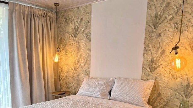 Una camera d'albergo con un letto grande, due comodini, un tavolino rotondo e una parete decorata con un motivo a foglia.