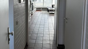 Ein Korridor mit Fliesenboden, einer Tür rechts und einem Fenster am Ende.
