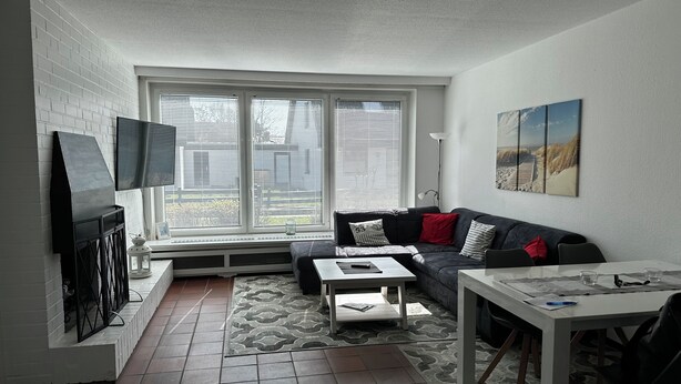 Ein Wohnzimmer mit Fernseher, Sofa, Couchtisch und Esstisch.