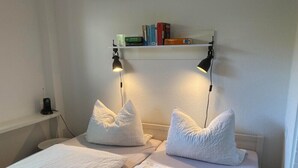Ein Schlafzimmer mit zwei Betten, jeweils mit weißer Bettwäsche und Kissen, einem Regal mit Büchern und zwei Wandlampen.