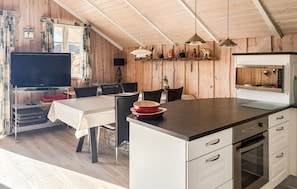 Une cuisine moderne avec un îlot central, un coin repas comprenant une table et des chaises, et un téléviseur posé sur une étagère.