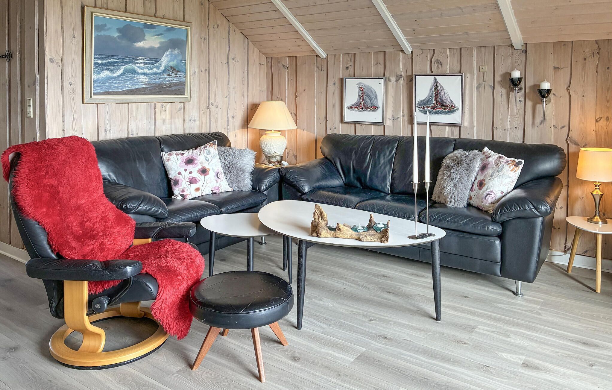 A cozy room with a black leather sofa, a red chair, a small round table, and a lamp.