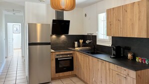 Eine moderne Küche mit Edelstahlkühlschrank, integriertem Backofen, schwarzem Arbeitsplatz, Holzschränken und einer Pendelleuchte.