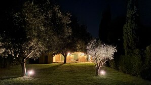 Ein Haus bei Nacht mit gut beleuchteter Rasenfläche, Bäumen und einer sichtbaren Terrasse.
