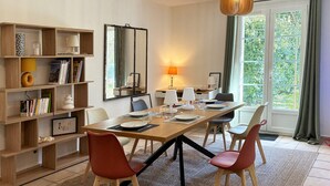 Ein Essbereich mit Holztisch, roten Stühlen, einem Bücherregal und einem großen Fenster mit Vorhängen.