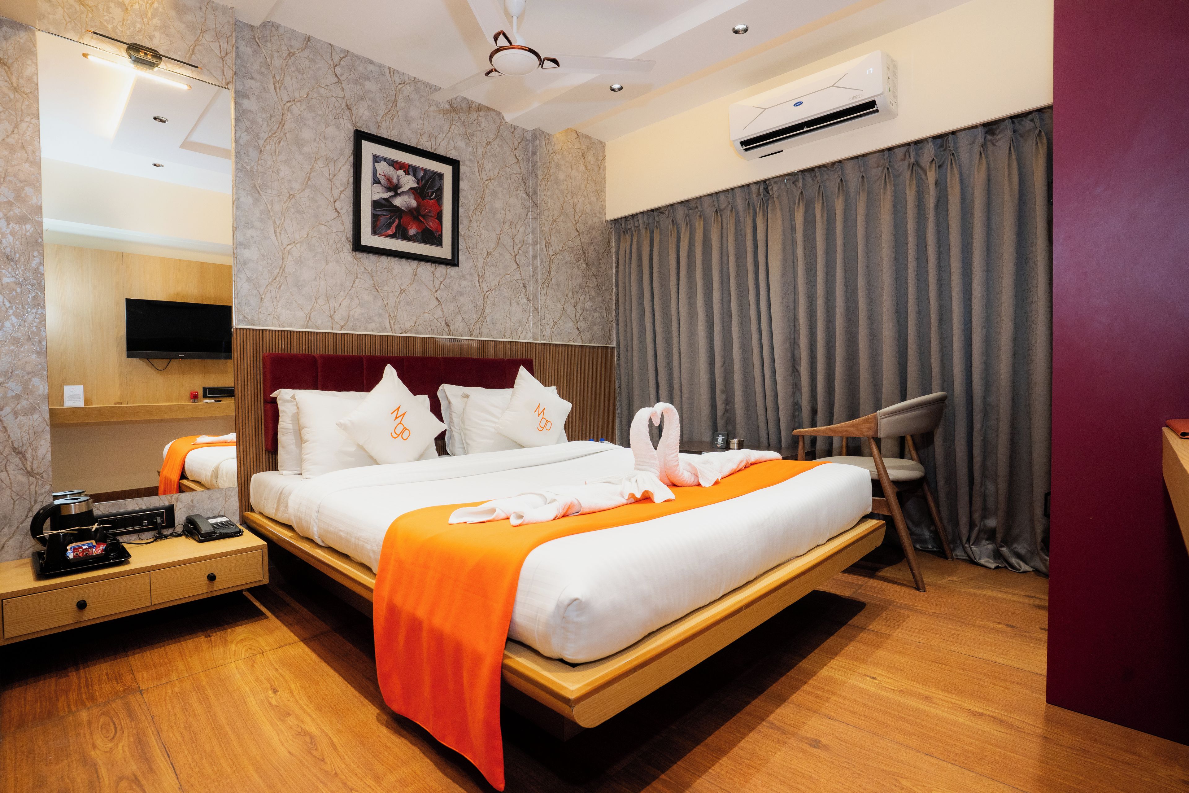 A hotel room with a bed, a bedside table, a TV, an air conditioning unit, and a large window with curtains.